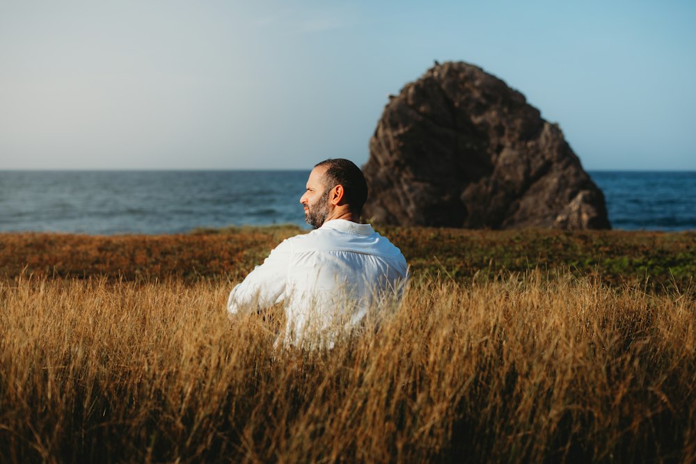 Man meditating in golden grass by the sea