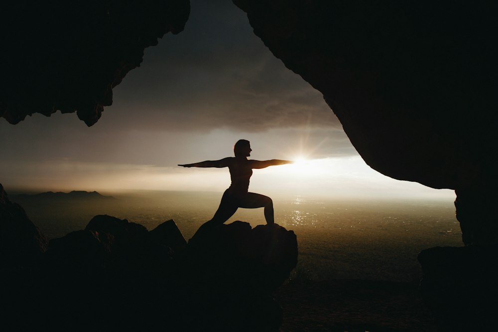 Silhouette of a person in a yoga pose on a cliff at sunset